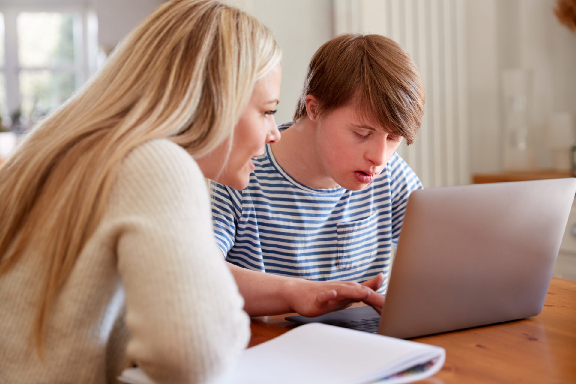 Down syndrome teen sitting at laptop with teacher at home