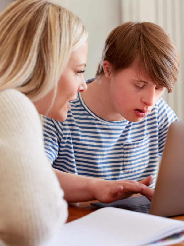 Down syndrome teen sitting at laptop with teacher at home